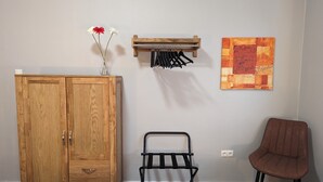 A room with a wooden wardrobe, a metal chair, a wall-mounted drying rack, and a painting.