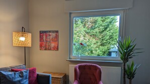 A living room with a sofa, a chair, a lamp, a window with a view of trees, and a potted plant. - Holiday Apartment "Goldgrube Attic" with Wi-Fi (Koblenz)
