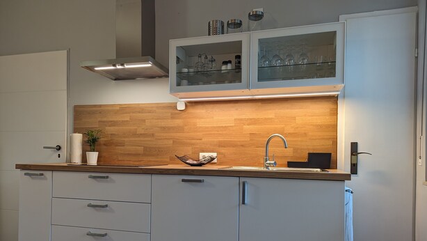 A modern kitchen with a wooden backsplash, a stainless steel sink, and white cabinetry. - Holiday Apartment "Goldgrube Attic" with Wi-Fi (Koblenz)