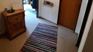 A hallway with a wooden dresser, a rug, a door, and wall-mounted decorations.