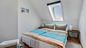 Un dormitorio con techo inclinado, tragaluz, cama con colcha estampada, mesita de noche con lámpara y una alfombra pequeña.