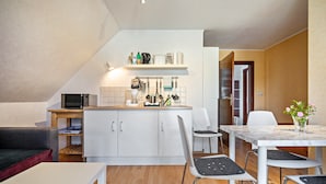 Una cocina funcional con microondas, armarios blancos y una zona de comedor con mesa y sillas.