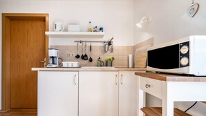 A kitchen with white cabinets, a coffee maker, a microwave, and a wooden door. - Apartment 'Ferienwohnung 2 Schulze' with Private Terrace, Shared Garden and Wi-Fi (Neustrelitz)