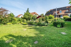 Un jardín residencial con césped, diversas plantas y una casa con paneles solares.