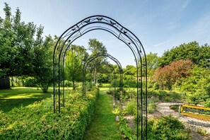 Un jardín con un arco de metal, un sendero y diversas plantas.