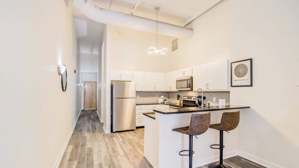 Una cocina moderna con armarios blancos, un refrigerador de acero inoxidable, un microondas y una isla grande con taburetes de bar.