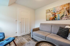 Un salon avec un canapé gris, un fauteuil bleu, une porte et un tableau représentant un cerf accroché au mur.