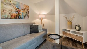 A modern living room with a grey sofa, a floor lamp, a side table, a white console table with a clock, and a large abstract painting on the wall. - Holiday Apartment "Am Wald Dachgeschoss" with Shared Terraces, Shared Garden & Wi-Fi (Krauschwitz)