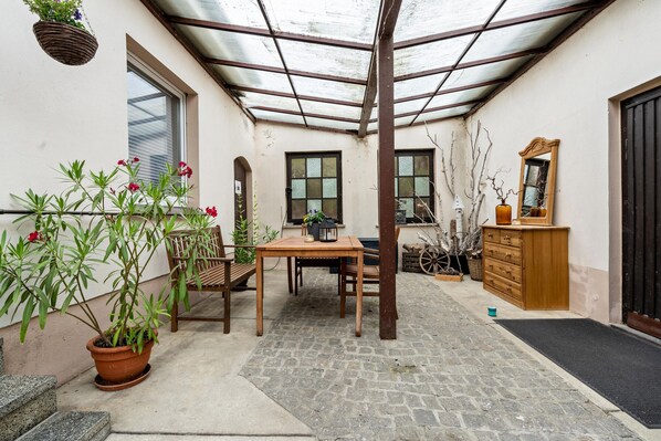 Un patio couvert avec une table et des chaises, des plantes en pot, une commode en bois et un miroir.