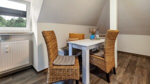 A small, triangular room with a white table and two wicker chairs, a radiator, and a window with blinds. - Holiday Apartment "Am Wald Dachgeschoss" with Shared Terraces, Shared Garden & Wi-Fi (Krauschwitz)