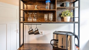 A kitchen with a coffee maker, hanging mugs, wine glasses, and a potted plant on shelves. - Holiday Apartment "Am Wald Dachgeschoss" with Shared Terraces, Shared Garden & Wi-Fi (Krauschwitz)