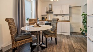 A modern kitchen with white cabinets, a stainless steel range hood, and a dining area with wicker chairs and a round table. - Apartment 'Fewo Am Wald Erdgeschoss' with Shared Terrace, Shared Garden and Wi-Fi (Krauschwitz)