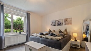 A bedroom with a bed, bedside table, lamp, and a window with curtains. - Apartment 'Fewo Am Wald Erdgeschoss' with Shared Terrace, Shared Garden and Wi-Fi (Krauschwitz)