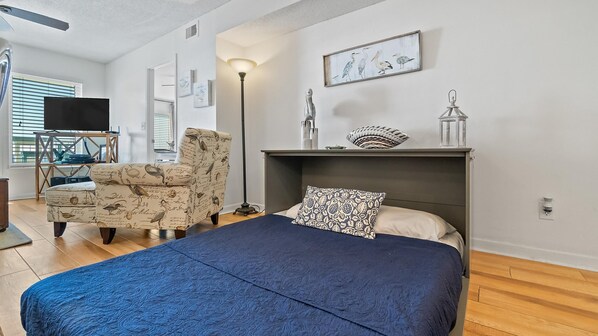 A bedroom with a bed, a chair, a lamp, and a wall-mounted shelf with decorative items.