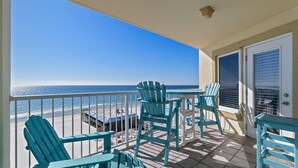 A balcony with turquoise Adirondack chairs, a small table, and a view of the beach and ocean. - Book Boardwalk 783 – Breathtaking Gulf Views Await! (Gulf Shores)