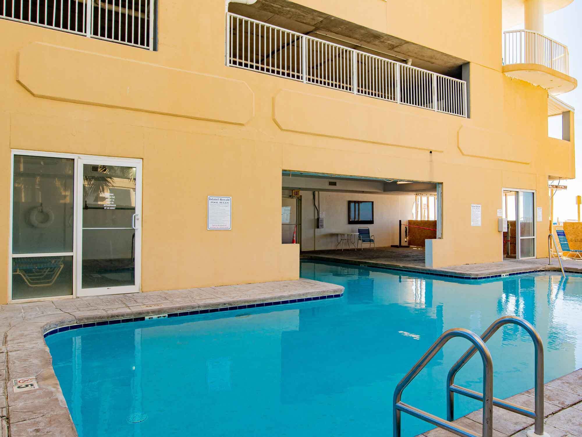 Una piscina con una escalera metálica, un área techada con mesa y sillas, y un cartel que indica las normas de la piscina.