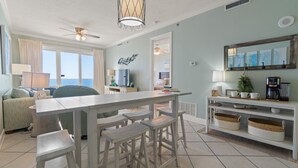 Una sala de estar moderna con comedor, ventilador de techo, ventanal y vista al océano.