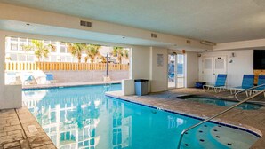 Una piscina interior con agua azul cristalina, una valla de madera en el exterior y varias sillas de descanso.