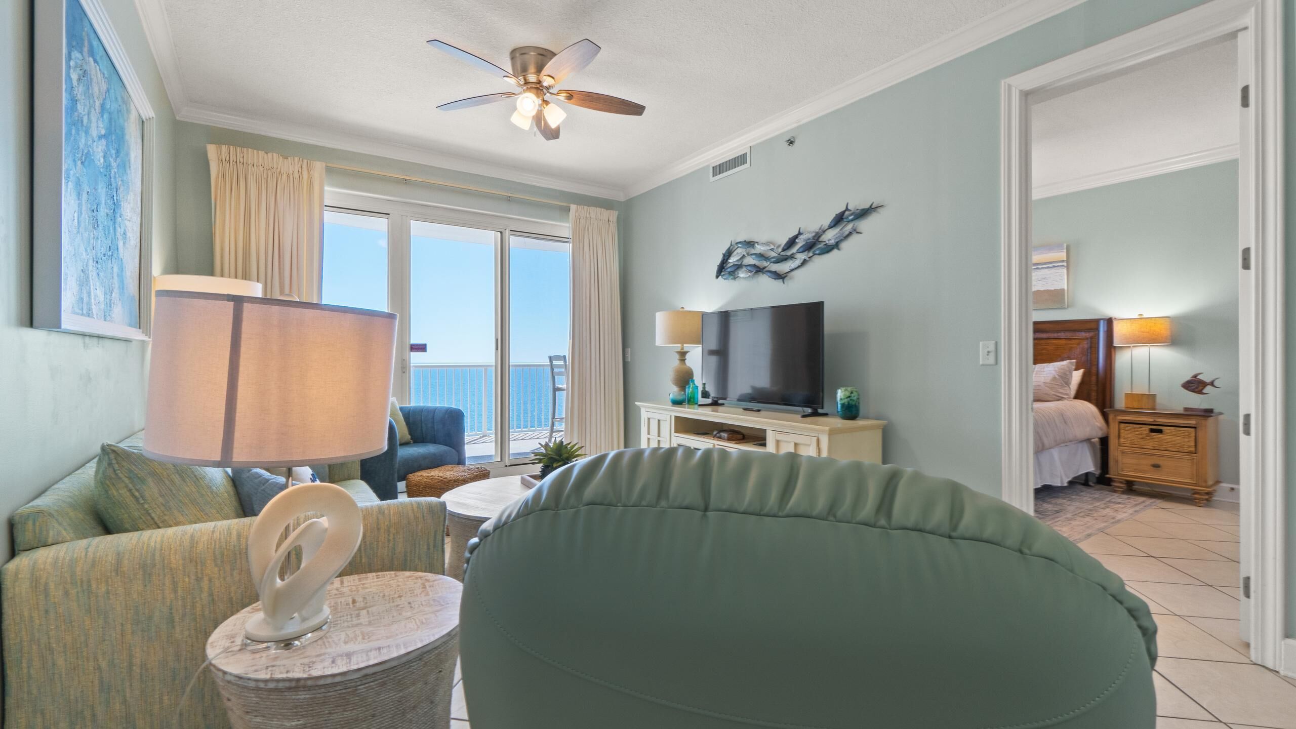 A room with a large window, a ceiling fan, a TV, a bed, and a nightstand.