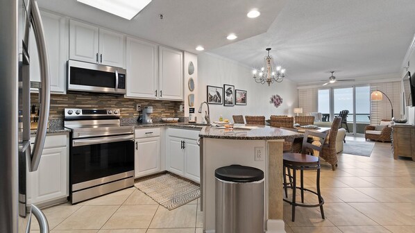 A modern kitchen with stainless steel appliances, a dining area with wicker furniture, and a view of the ocean.