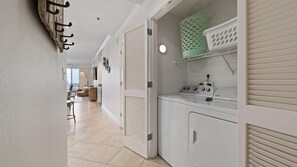 A laundry room with a Whirlpool washer and dryer, a shelf with laundry baskets, and a door with a coat rack.