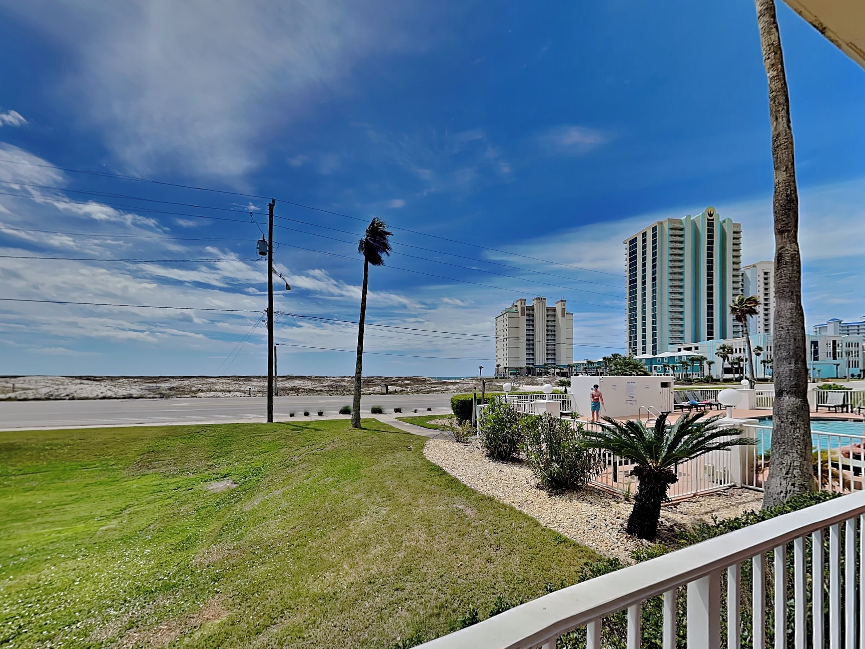 Un hotel frente al mar con piscina, palmeras y edificios altos al fondo.