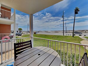A balcony with a table and bench, overlooking a road with vehicles and a clear sky. - Grand Beach Resort #109 | Pool + Across from Beach (Gulf Shores)