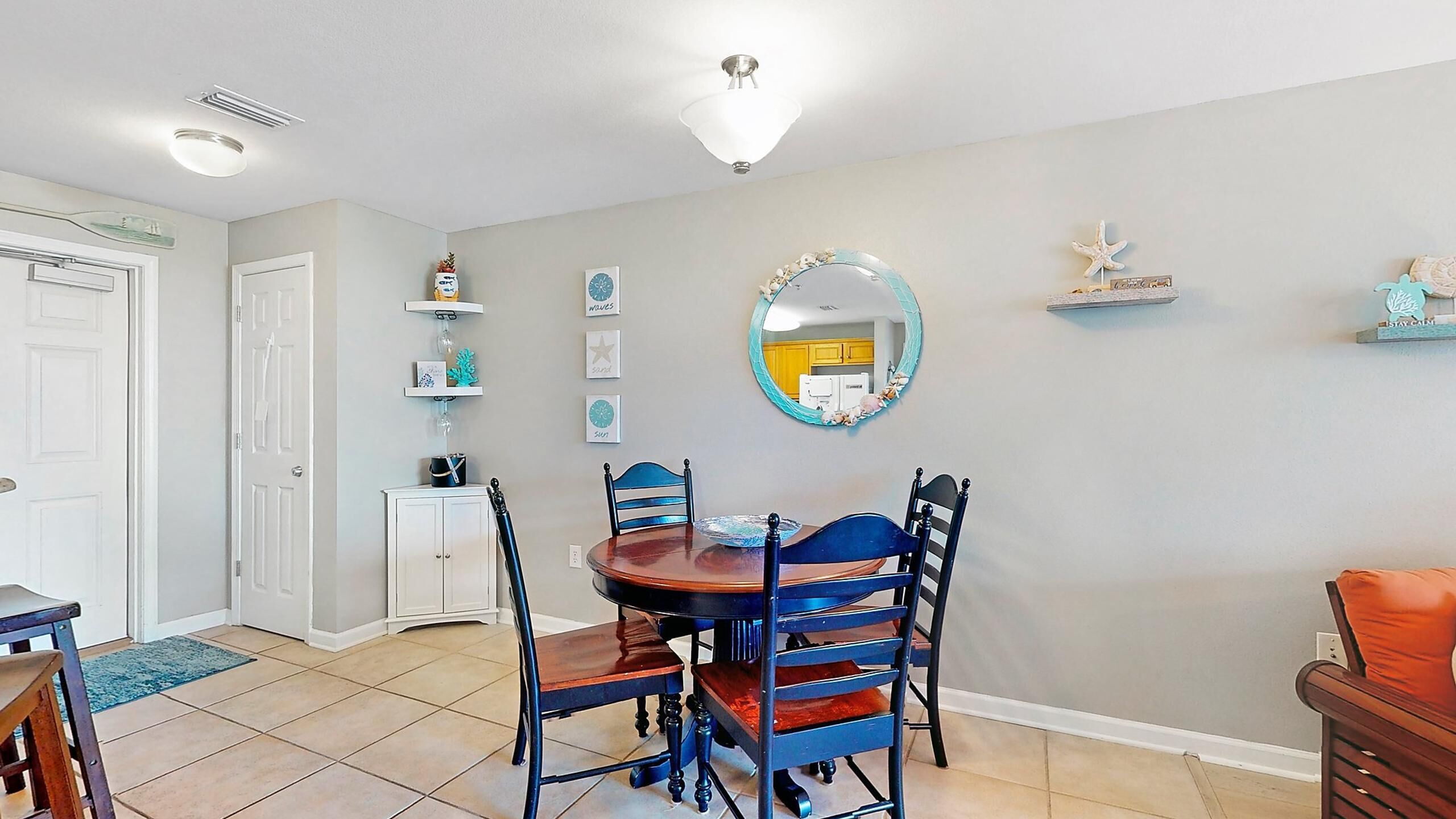 Un comedor con una mesa redonda y sillas, un espejo en la pared, y una cocina visible al fondo.