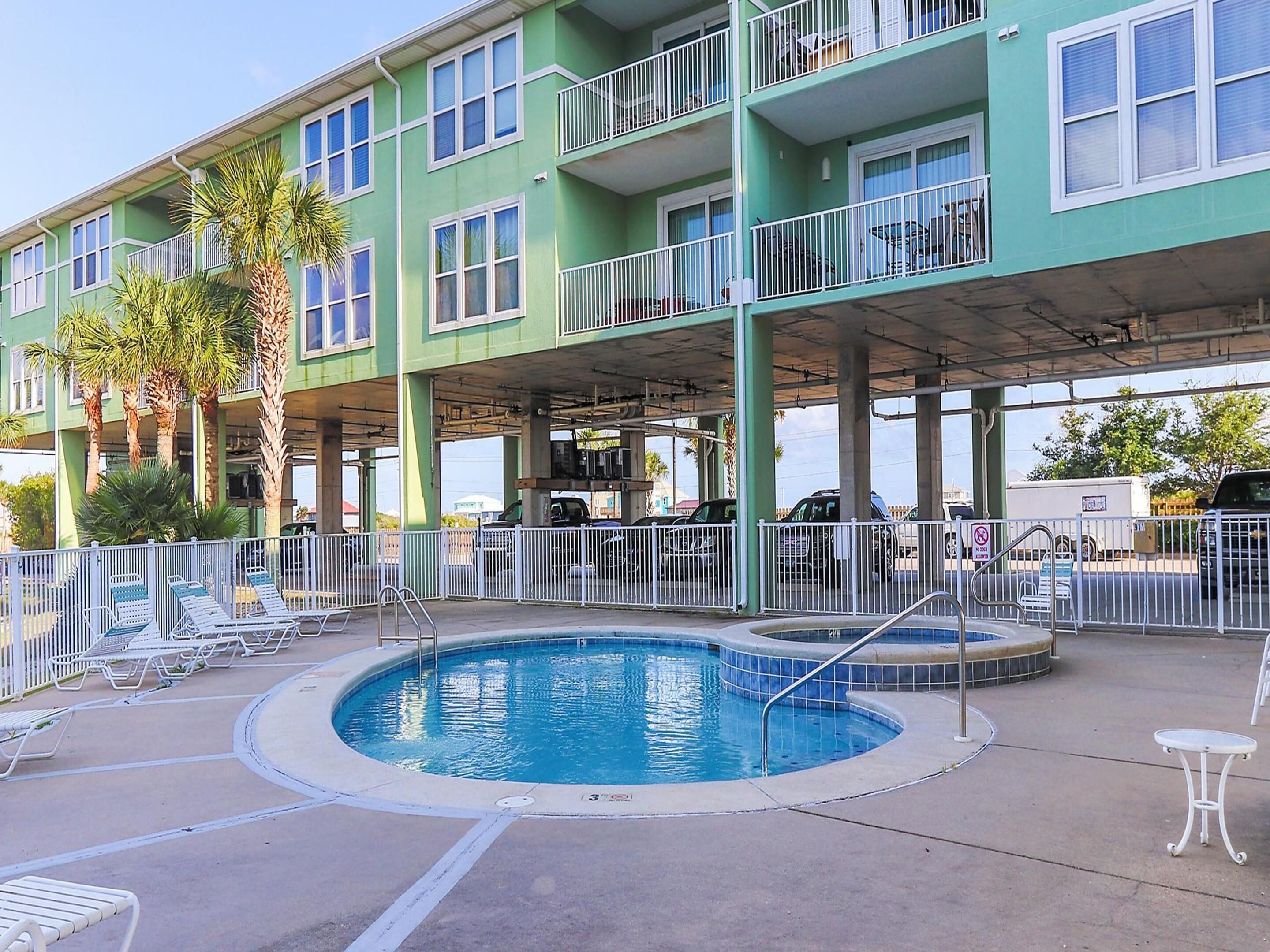 A multi-story building with a swimming pool, outdoor seating, and a covered parking area.