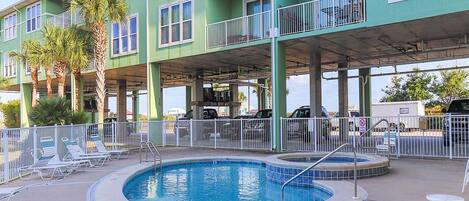 A multi-story building with a swimming pool, outdoor seating, and a covered parking area.