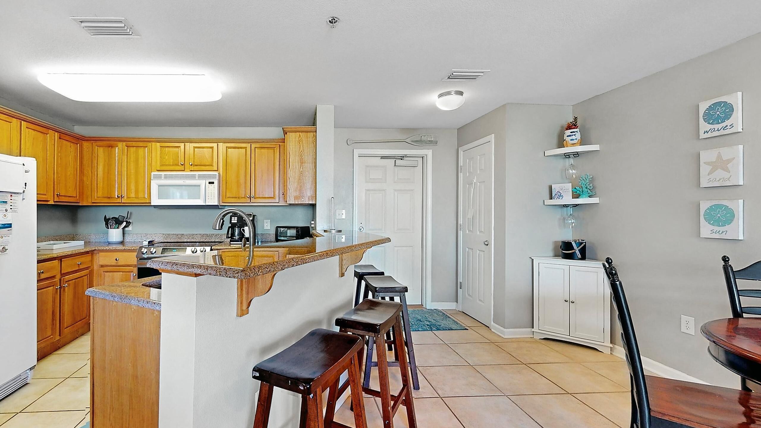 A kitchen with wooden cabinets, a microwave, a coffee maker, and a bar stool.