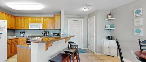 A kitchen with wooden cabinets, a microwave, a coffee maker, and a bar stool.