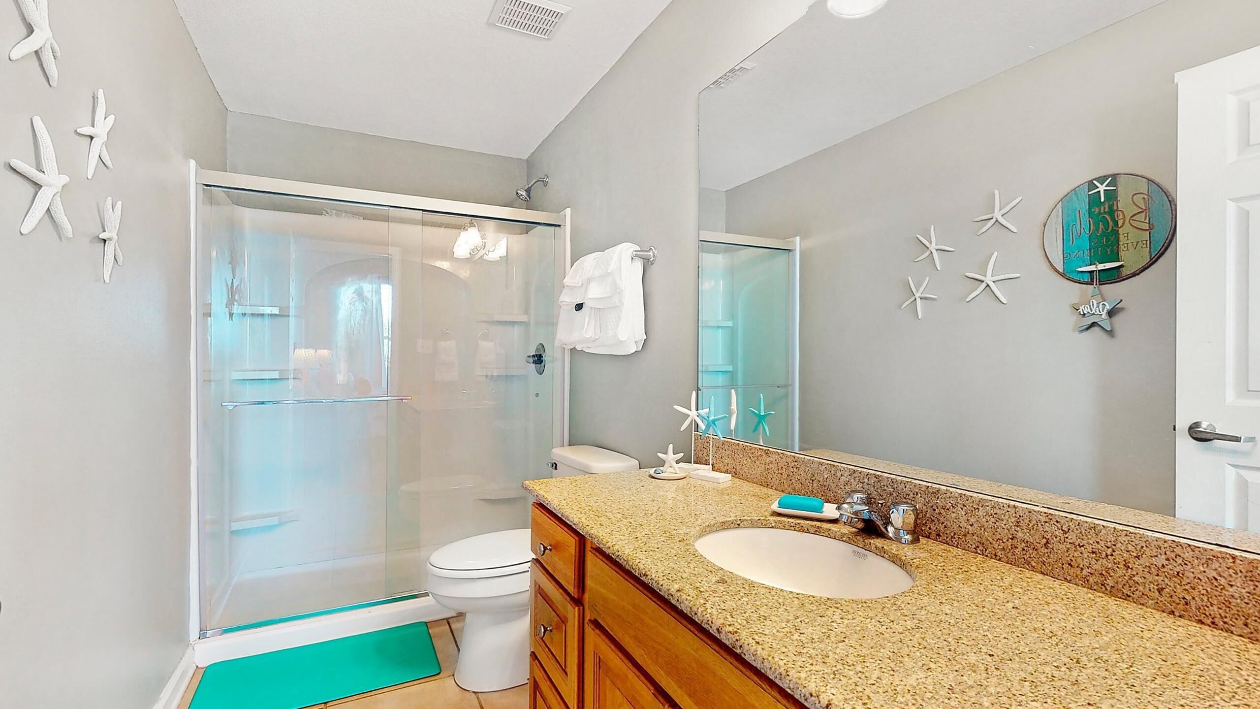 A bathroom with a glass shower enclosure, a toilet, a sink with a granite countertop, and a large mirror.