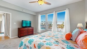 Un dormitorio con cama, televisor en una cómoda y vistas a una piscina a través de amplias ventanas.
