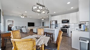 A modern kitchen with white cabinets, a stainless steel refrigerator, and a microwave. There is a dining area with a table and chairs. - Private Pool – Perdido Bay Views – Pet-Friendly Escape! (Elberta)