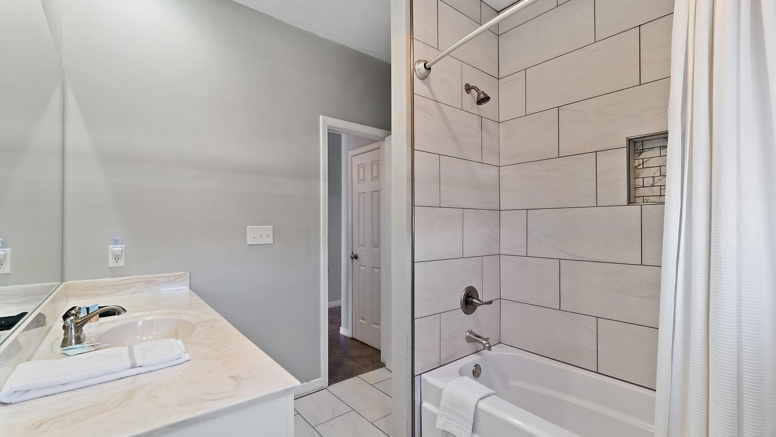A modern bathroom with a marble countertop, a shower with a glass door, and a visible door leading to another room.