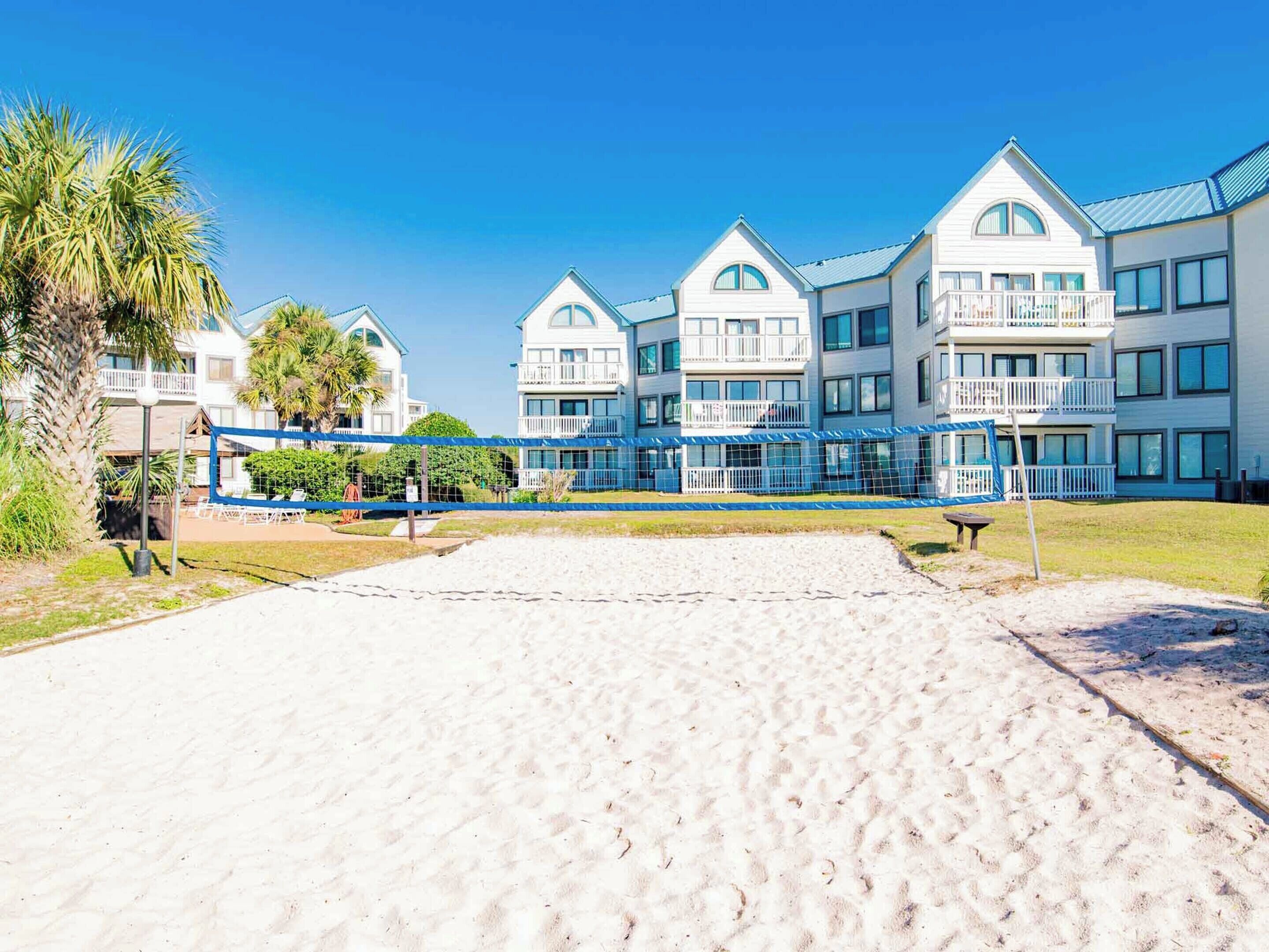A beachfront hotel with multiple-story buildings, a sandy beach in the foreground, and a clear blue sky.