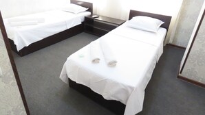 A hotel room with two single beds, each with white linens and pillows, a small bedside table with a lamp, and a plain wall with a subtle pattern. - Zamona Hotel (Tashkent)