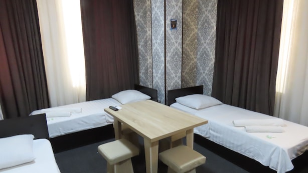 A hotel room with two single beds, a small wooden table with two stools, and a mirror on the wall. - Zamona Hotel (Tashkent)
