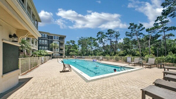 A rectangular swimming pool with a tiled deck, surrounded by lounge chairs and a fence.