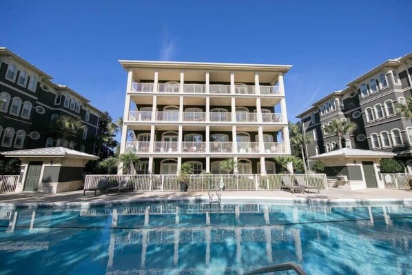 A multi-story hotel with a central pool area, balconies on each floor, and a clear blue sky.