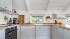 Une cuisine moderne avec des meubles blancs, un four encastré, une machine à café et une fenêtre donnant sur un paysage verdoyant.
