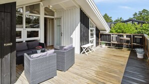 Un espace extérieur abrité, aménagé avec des meubles en osier, une table et des chaises, ainsi qu’une terrasse en bois.