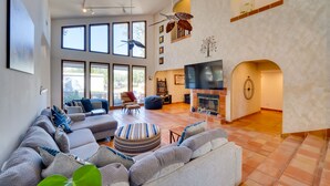 A spacious living room with a large sectional sofa, a round ottoman, and a fireplace. There are multiple windows providing natural light and a ceiling fan. - 1-Acre Backyard & Gym: Spacious Apopka Escape! (Apopka)