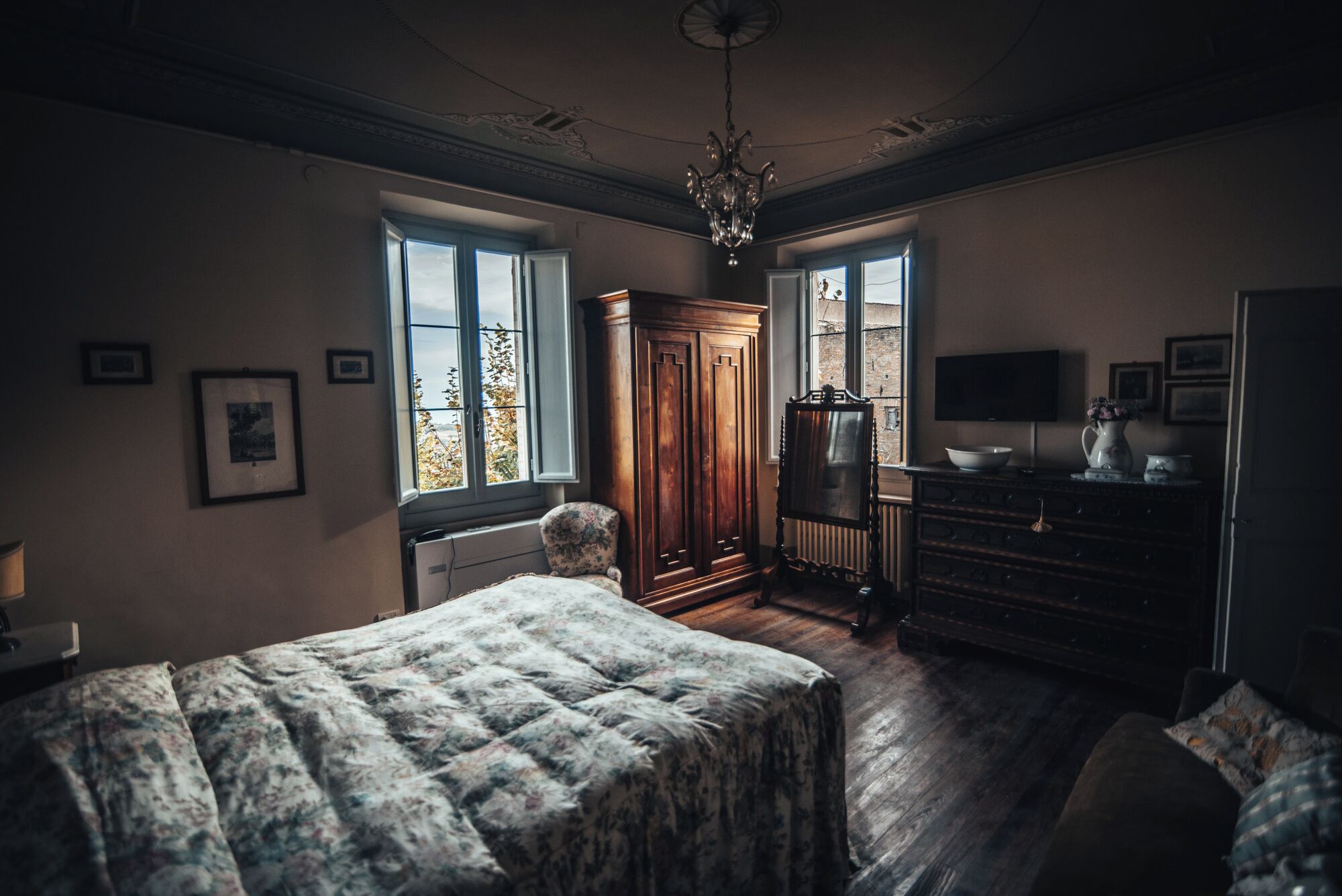 A bedroom with a large bed, a wooden wardrobe, a dresser, and a television.