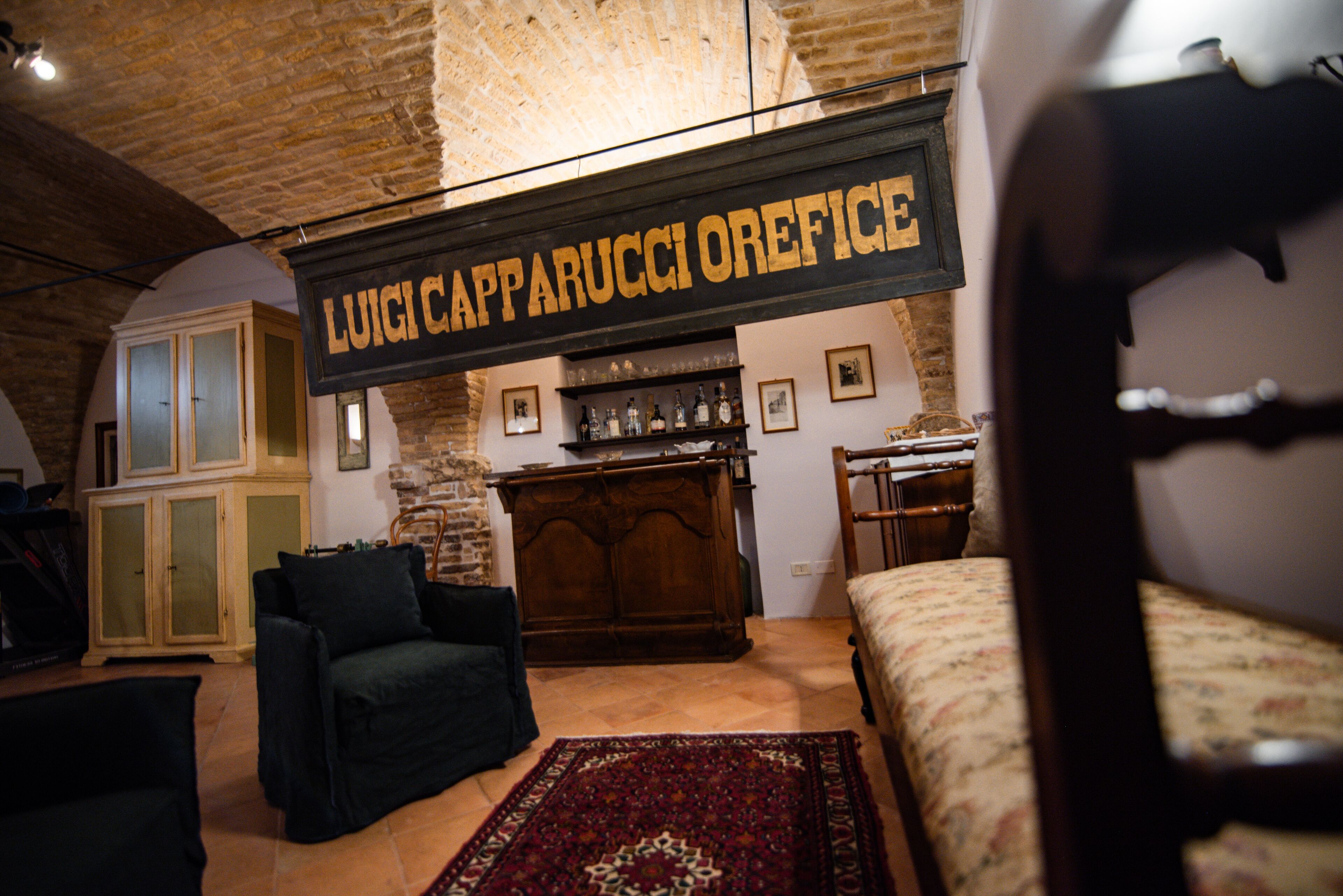 Una habitación rústica con una cama, un sillón oscuro, un armario de madera y un letrero que dice "LUIGI CAPPARUCCIOREFICE".