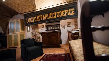 Una habitación rústica con una cama, un sillón oscuro, un armario de madera y un letrero que dice "LUIGI CAPPARUCCIOREFICE".