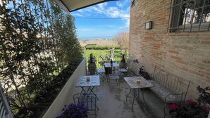 Eine überdachte Terrasse mit Tischen und Stühlen, eine Backsteinmauer und Blick auf die Landschaft.