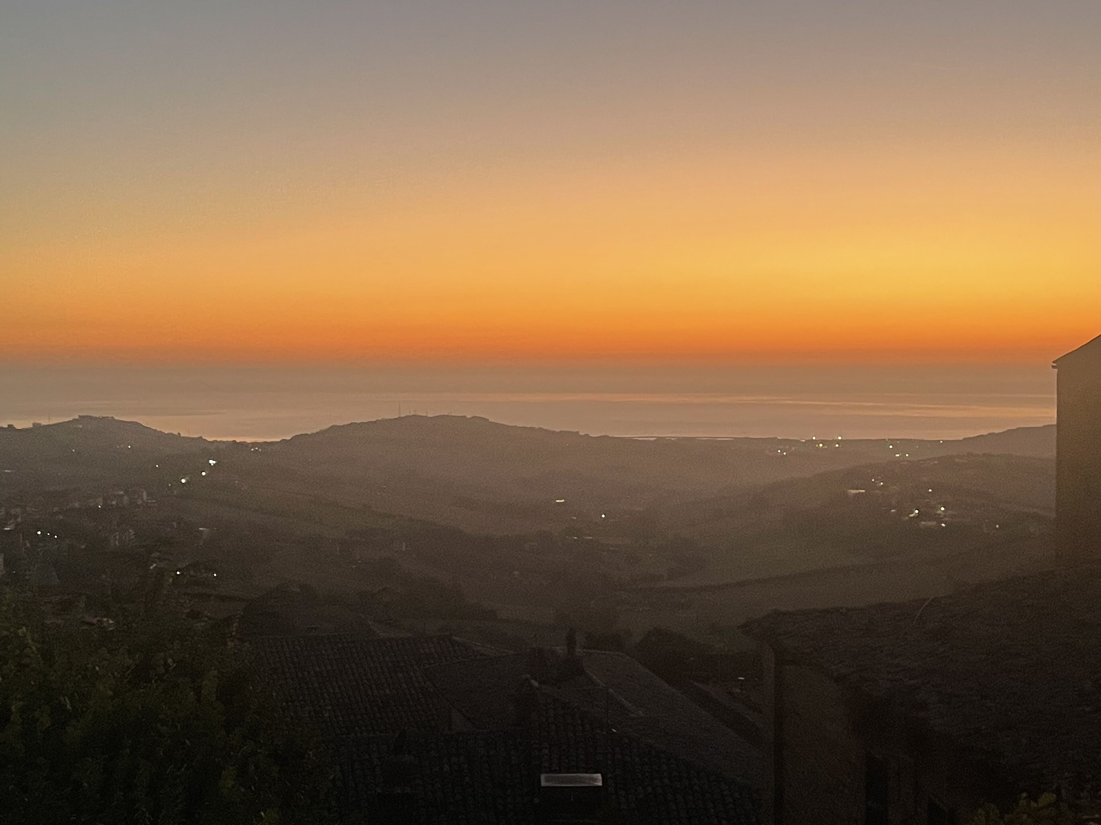 Vista panorámica de un paisaje costero al atardecer, con luces de la ciudad a lo lejos.