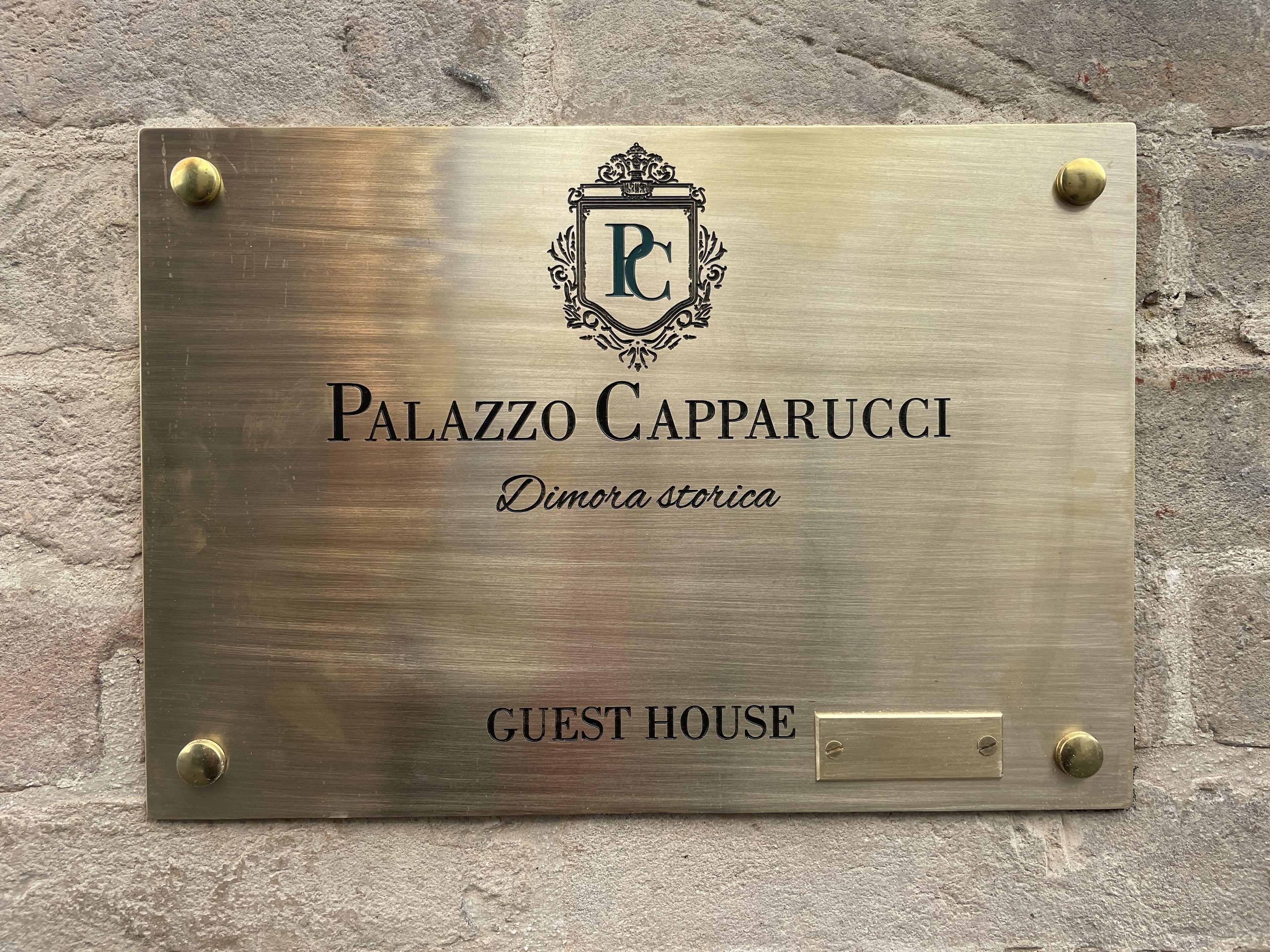 Une plaque portant l’inscription « Palazzo Capparuci » et « Maison d’hôtes » est fixée à un mur à texture.